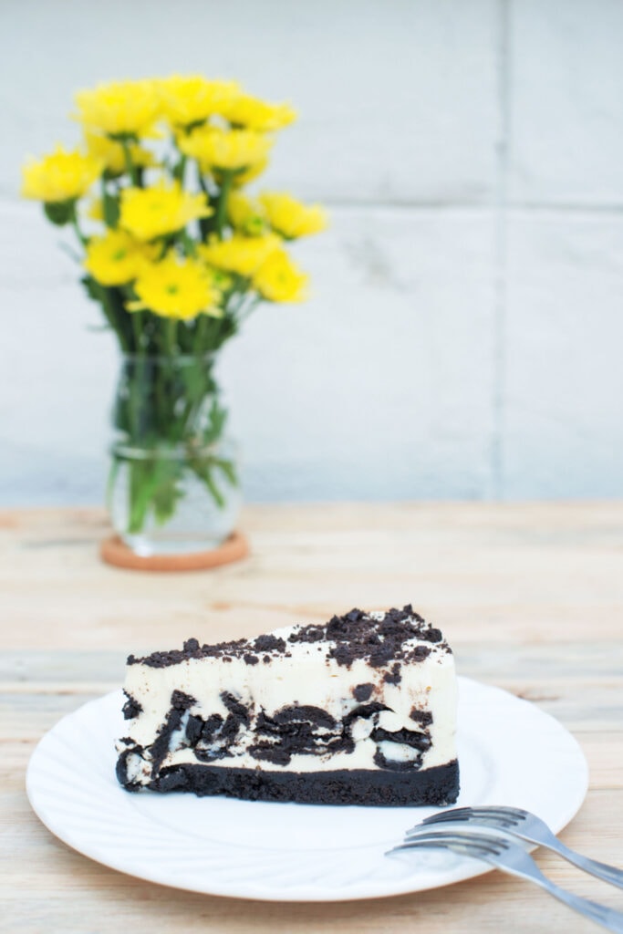 Philadelphia Oreo Cheesecake on a white plate with a vase of flowers in the background