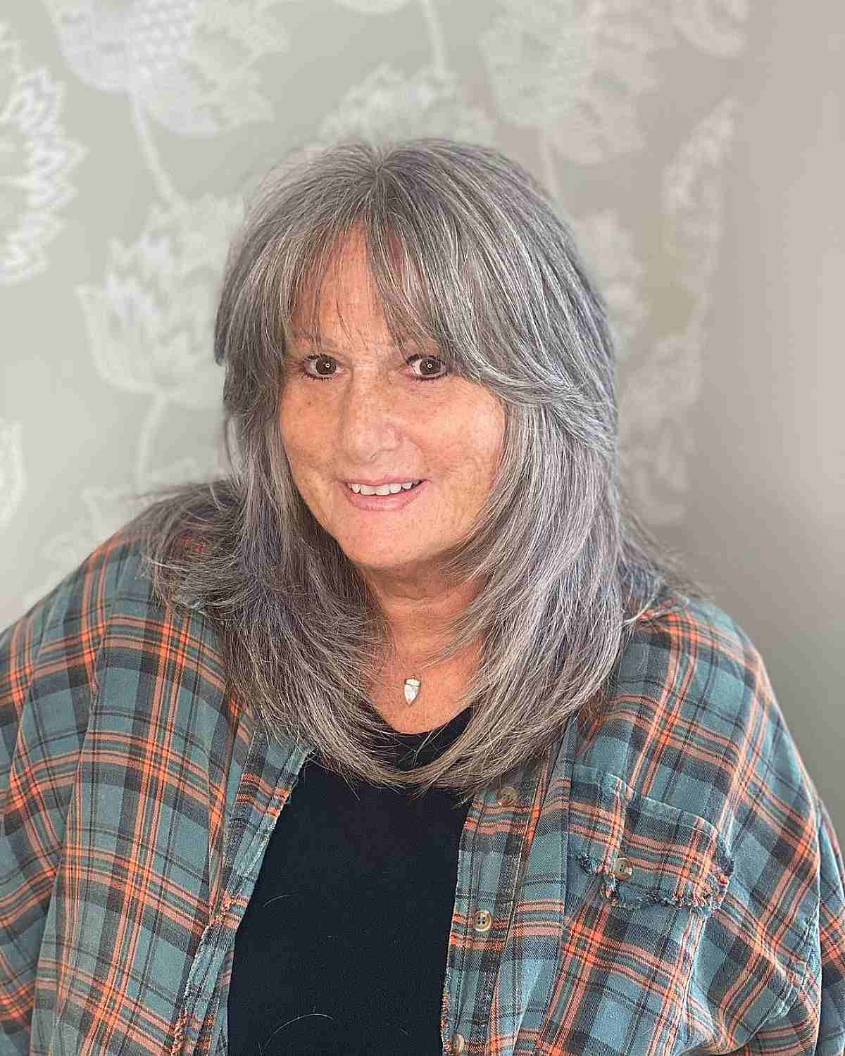 Frange de rideau à plumes légères et couches rasées sur les cheveux gris pour une femme de plus de 60 ans