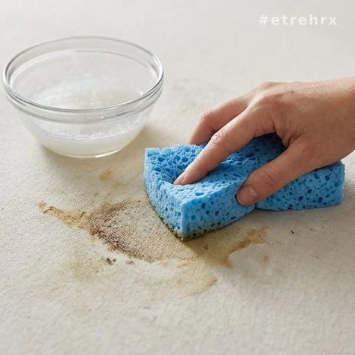 Éponge essorée appliquée sur une tache de matelas avec mélange vinaigre blanc et eau tiède