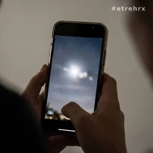 Mains tenant un smartphone avec photo d'un phénomène lumineux non identifié dans le ciel